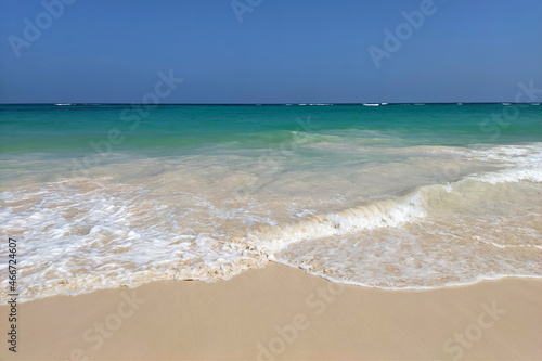 Surf on a tropical sandy beach, scenic view to empty sea coast with white sand and azure wave with white foam. Picturesque seascape with blue sky © Oleg