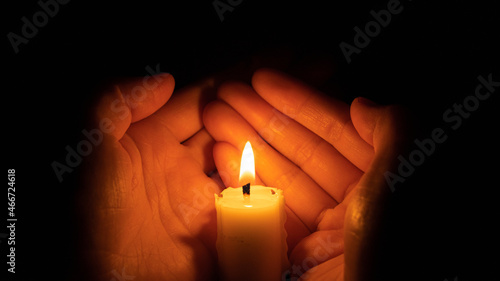 Two hands holding burning candle in darkness, closeup