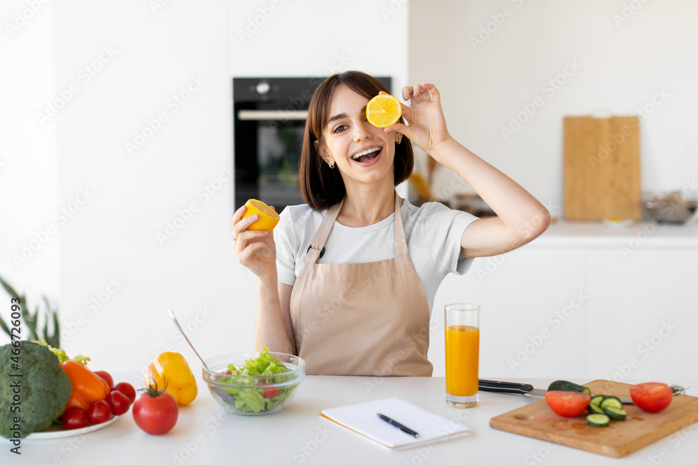 Playful young woman having fun and covering her eyes with lemon slices, fooling around in kitchen interior Playful young woman having fun and covering her eyes with lemon slices, fooling around in kitchen interior