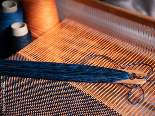 Billede på lærred Creation of the blue and orange textile using weaving loom