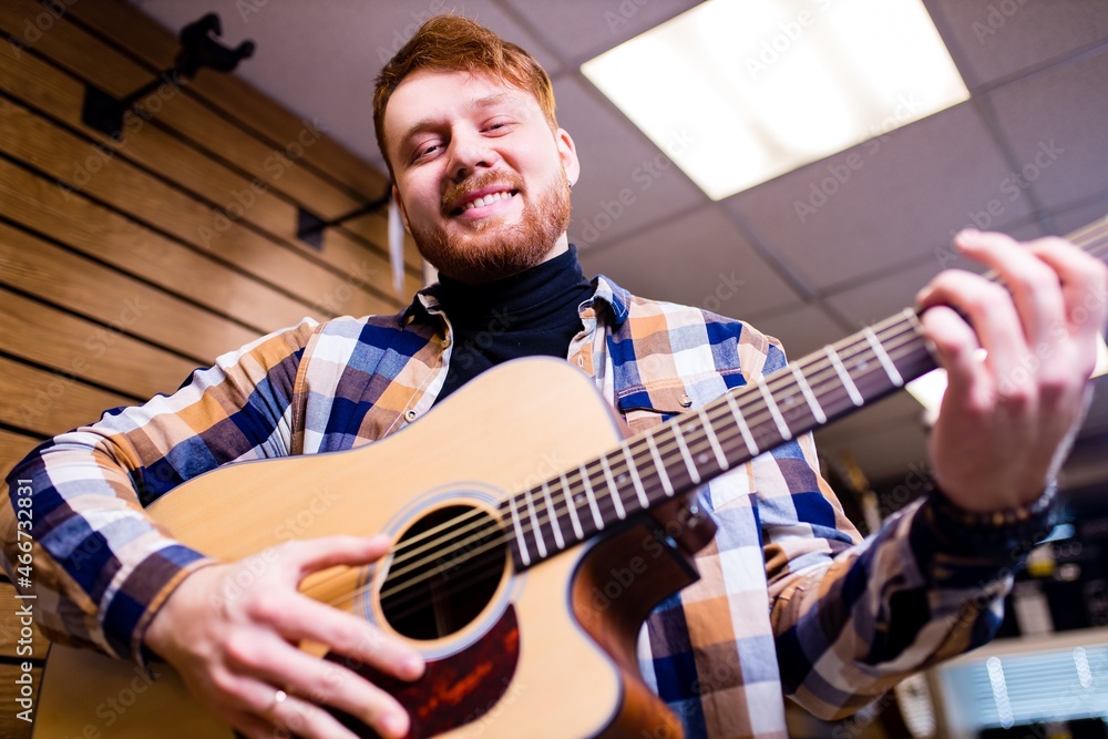 Obraz premium Man with red ginger hair and beatd is considering a guitars in a music store