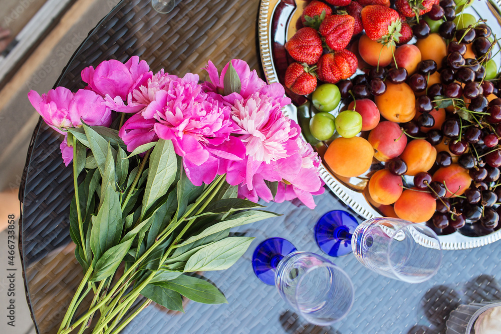 Summer picnic on the terrace with strawberries, cherries, peaches, marshmallows, peonies and a bottle of champagne and two glasses. Beautiful decor.