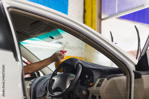 Man specialist spraying water into tinted car window in garage.