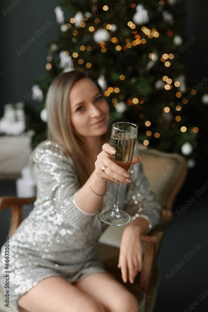 A young woman in a short dress keeps a glass of champagne and makes a cheers gesture