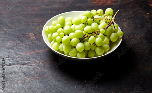 Branch of ripe green grape on plate. Juicy grapes on wooden background, closeup. Grapes on dark kitchen table with copy space