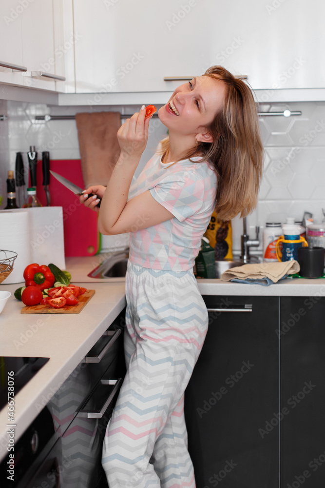 A joyful young woman, cutting a salad in her kitchen, shows a sweet red pepper close-up. Cooking healthy and healthy food