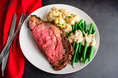 Prime Rib Served with Garlic Mashed Potatoes and Green Beans: Medium-rare prime rib dinner served with side dishes on a white plate photo