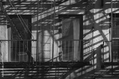 New York City tenement style apartment building windows with fire escape casting long intricate shadows or the early morning sunlight 