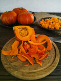 Orange little pumpkins for cooking dishes and recipes on a wooden board and a dark table, cut into pieces