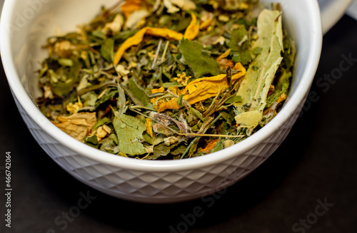 herbal tea leaves on black background or in white ceramic cup.tea from natural herbs harvested in own garden,natural, eco,ecological product.top view.night tea for insomnia,calm,relaxation,bio leaves.