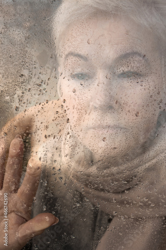Portrait of an older beautiful woman at the window with raindrops