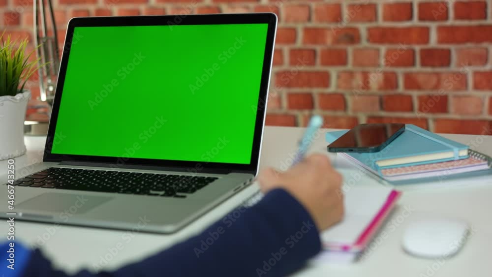 Closeup of young student using a digital tablet while studing at home. Scrolling on a green screen. Distance learning. Closeup of young student using a digital tablet while studing at home. Scrolling on a green screen. Distance learning.