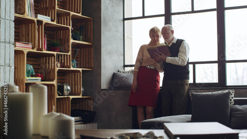 Картината върху платно Senior couple reading book together in living room