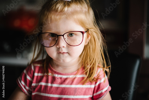 Happy small blonde girl looking in camera with happy and peaceful expression in brand new glasses.