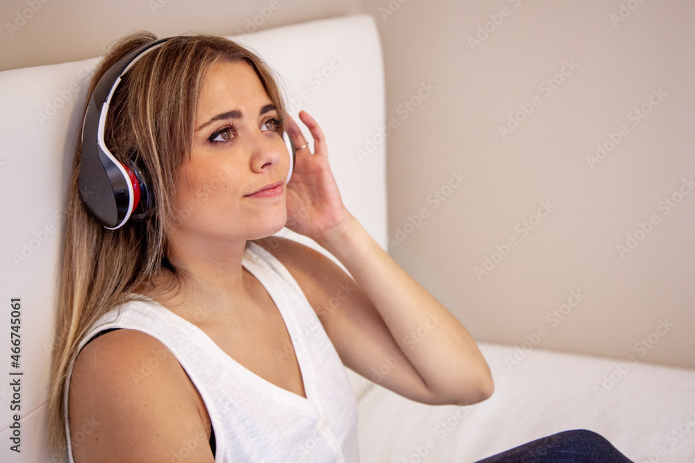 Naklejka premium Mujer escuchando música con auriculares sentada en la cama de su habitación. 