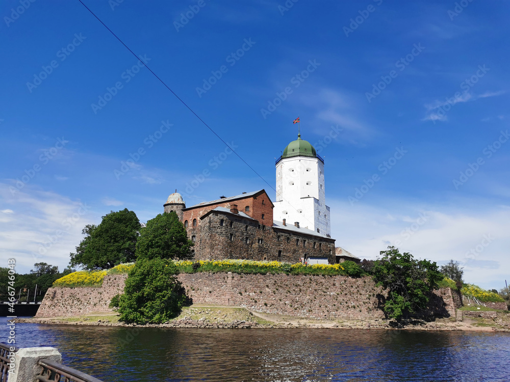 View from the embankment of the Vyborg Castle and the St. Olaf Tower, built in the 13th century, in the city of Vyborg against the blue sky. View from the embankment of the Vyborg Castle and the St. Olaf Tower, built in the 13th century, in the city of Vyborg against the blue sky.