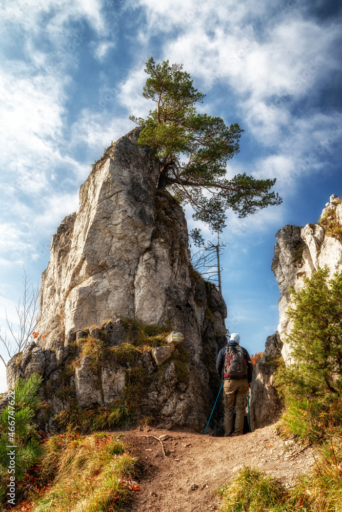 Hiker with trekking poles walking between rock formations on mountain path