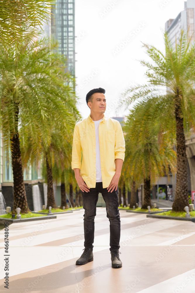 Full length portrait of handsome young man outdoors in city during summer thinking