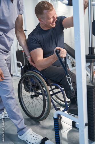 Young man with sport injury exercises with weight on tether machine