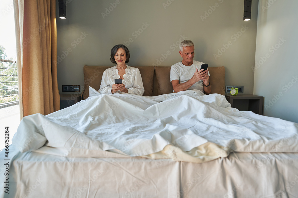 Pleased pensioners in bedroom using their smartphones