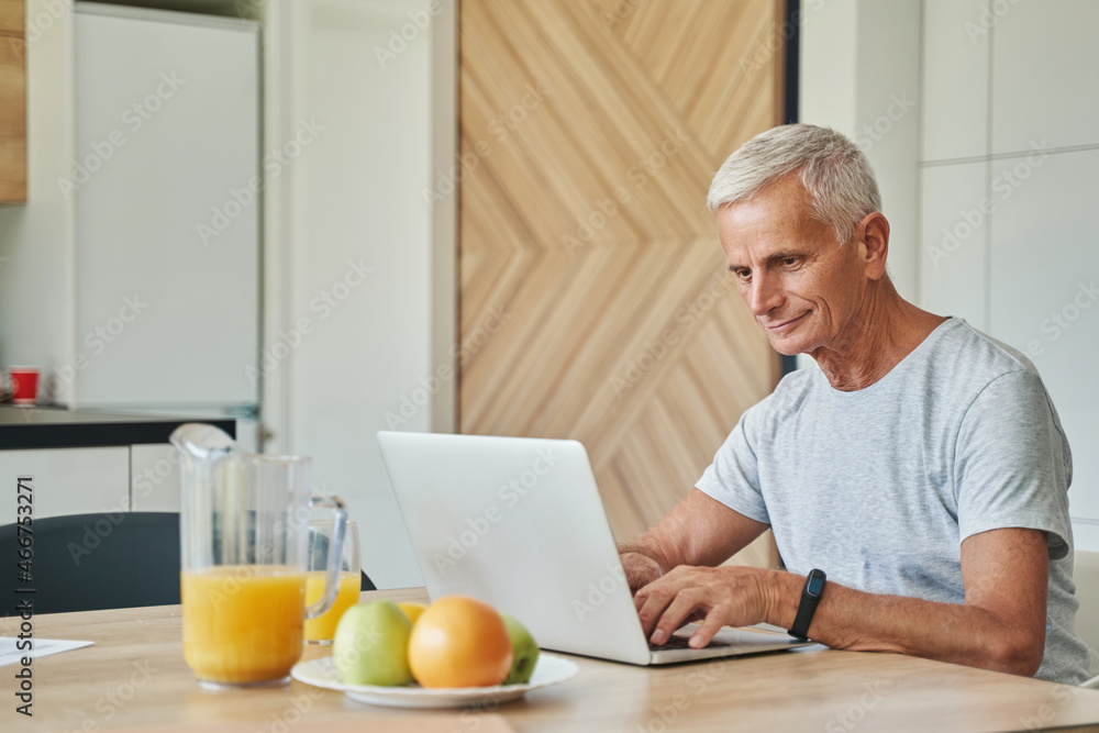Man pensioner clicking on laptop at kitchen table Man pensioner clicking on laptop at kitchen table
