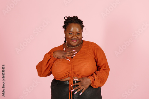 Attractive young black plus size body positive woman poses for camera on pink background in studio closeup