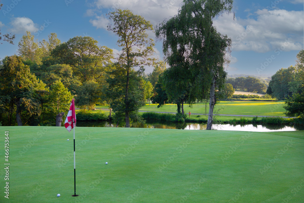 Obraz premium On the green, golf balls sit near the flag on the green at golf course as players hit their balls to try and obtain the treasured hole in one at the sport of golf.