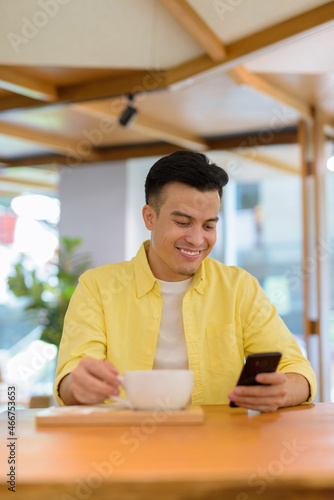 Portrait of handsome young man at coffee shop smiling and using mobile phone
