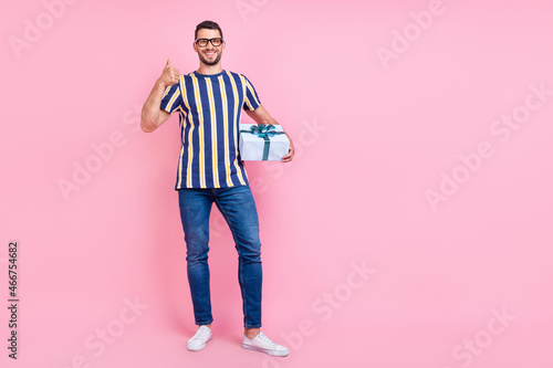 Full length millennial brunet guy hold present show okey wear t-shirt jeans sneakers isolated on pink background