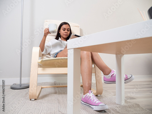 Young woman at home tired from work with a tablet sitting on a chair with a table in front of her in a relaxed atmosphere and drinking tea