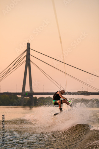 energy man holds rope and skilfully jumps on wakeboard on city bridge background.