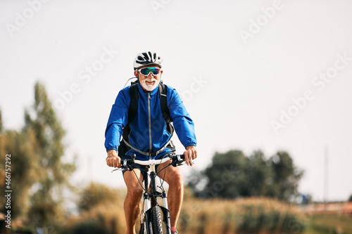 Happy senior athlete enjoys while riding bicycle in nature. photo