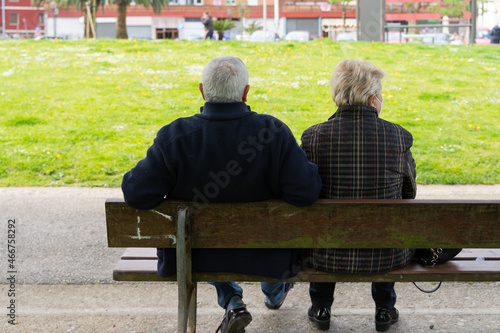 Senior couple sitting on bench from behind. Anonymous retired husband and wife in the park