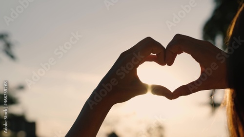 Girl made love heart out of her palms. Young Woman enjoying summer, relaxing. Carefree happy girl making heart shape with fingers. Light of summer spring sun on hands. Travel and relax in nature
