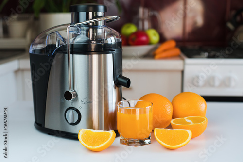 Modern juicer, glass of fresh orange juice and oranges on the table in the kitchen. Natural and healthy juices. Close-up. photo