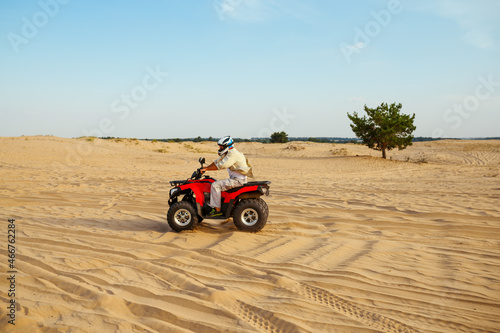 Man in helmet rides on atv in desert sands