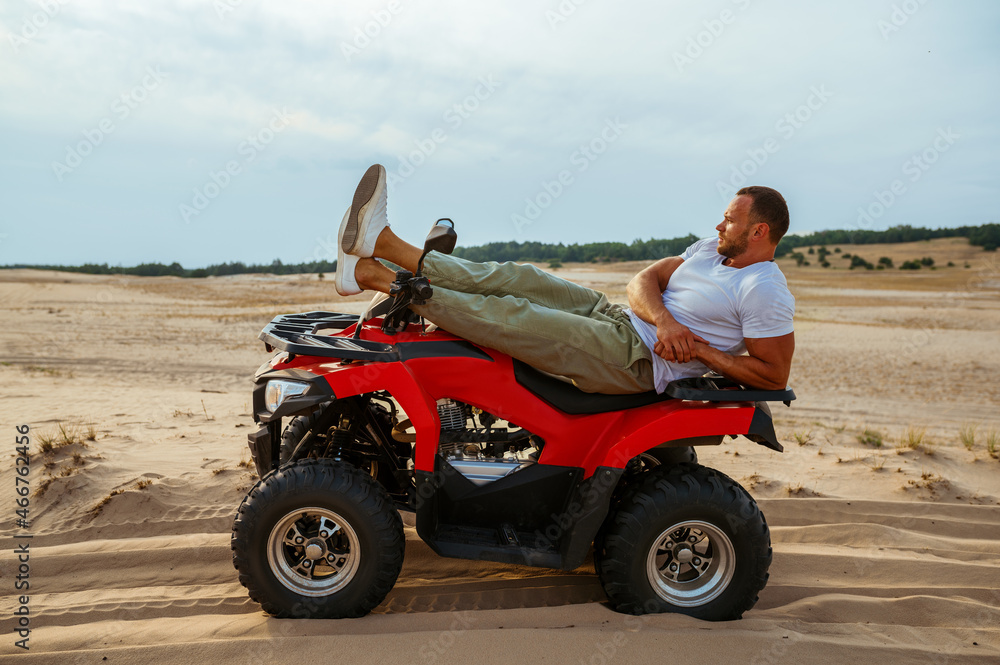 Brutal man lying on atv in desert, side view Brutal man lying on atv in desert, side view