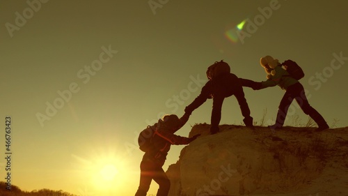 Travelers climb one after another on the rock. Teamwork of business people. Climbers silhouettes stretch their hands to each other, climbing to the top of hill. A team of businessmen is going to win.