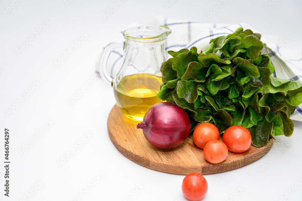 a bunch of green salad, tomatoes, olive oil, ed onion on the wooden board on white background. Ingridients for salad. a bunch of green salad, tomatoes, olive oil, ed onion on the wooden board on white background. Ingridients for salad.