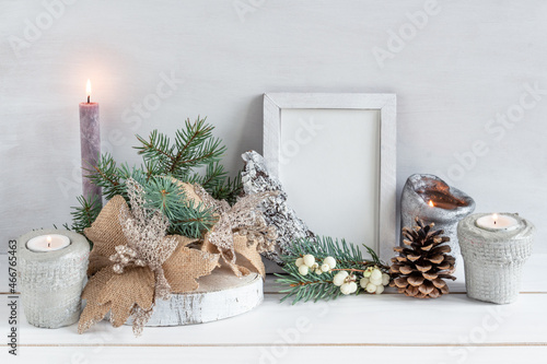 Christmas decoration, white frame mockup with a bouquet of fir, candle and christmas balls on a white table, copy space