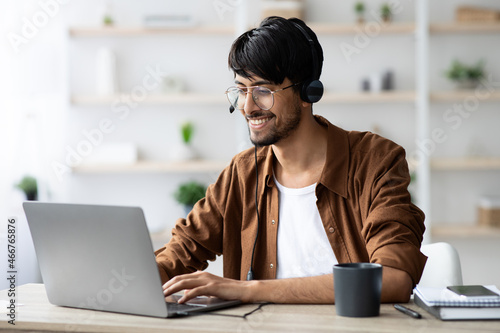 Happy indian guy attending webinar, typing on laptop keyboard