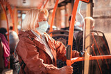 Adult 40-50 year old female passenger wearing a surgical mask on a subway train or bus transport while traveling in city during Covid 19
