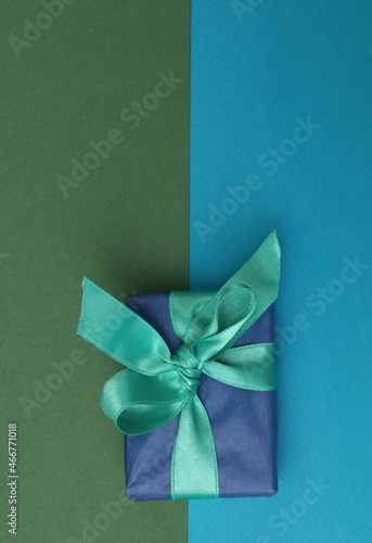 A top view of a gift box with a ribbon lying on a blue-green background.