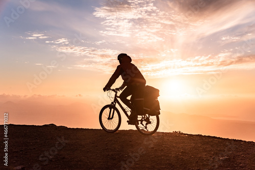 Mountain bicycle rider with backpack travels over sunrise background