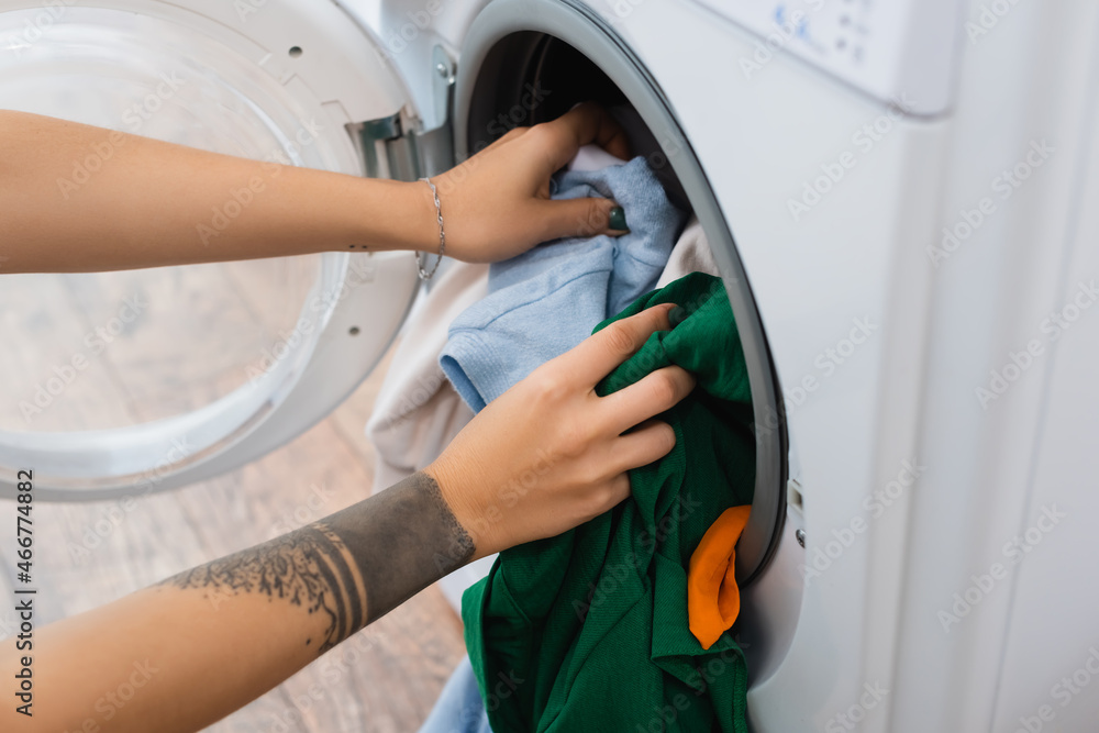 partial view of tattooed woman putting laundry into washing machine. partial view of tattooed woman putting laundry into washing machine.