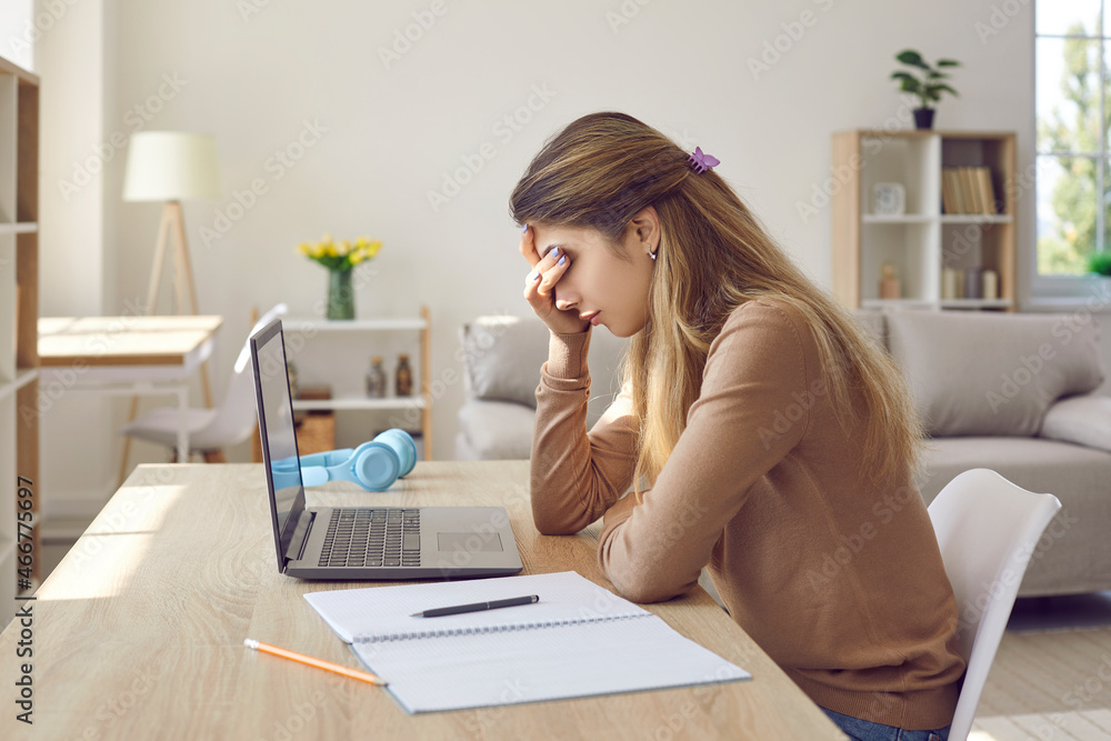 Bored frustrated female student tired of studying, working on laptop or sitting at home. Lazy apathetic and demotivated girl sitting at table and closes her eyes with her hand feeling disinterested. Bored frustrated female student tired of studying, working on laptop or sitting at home. Lazy apathetic and demotivated girl sitting at table and closes her eyes with her hand feeling disinterested.