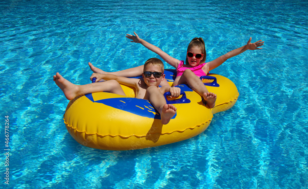 Boy and girl on inflatable float in outdoor swimming pool.