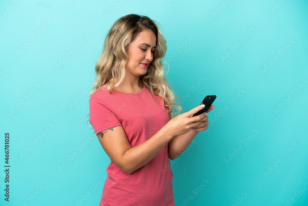 Young Brazilian woman isolated on blue background sending a message or email with the mobile Young Brazilian woman isolated on blue background sending a message or email with the mobile