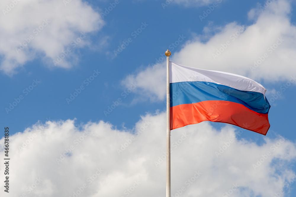 The flag of Russia flutters in the wind on a sunny day. Flag of the Russian Federation on a pole against the sky with clouds. Waving Russian tricolor. Copy space