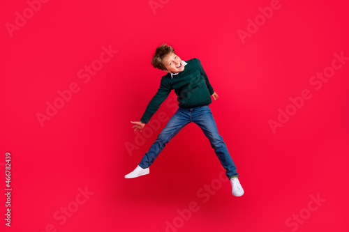 Photo of pretty funny school boy wear knitted pullover smiling jumping high isolated red color background